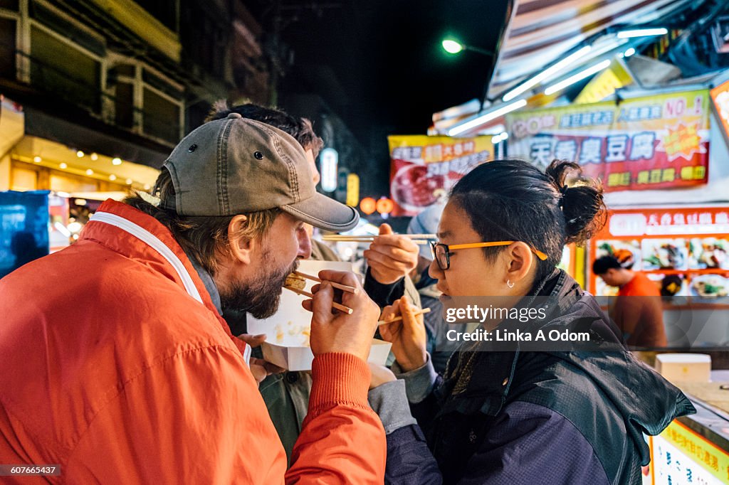Friends eating with chopsticks Asian night market