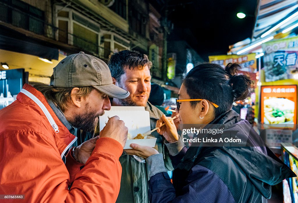 Friends eating with chopsticks Asian night market