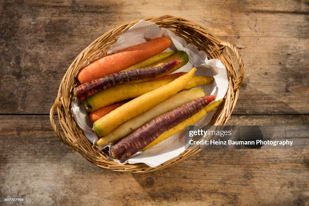 Different colored carrots in a basket on a weathered garden table