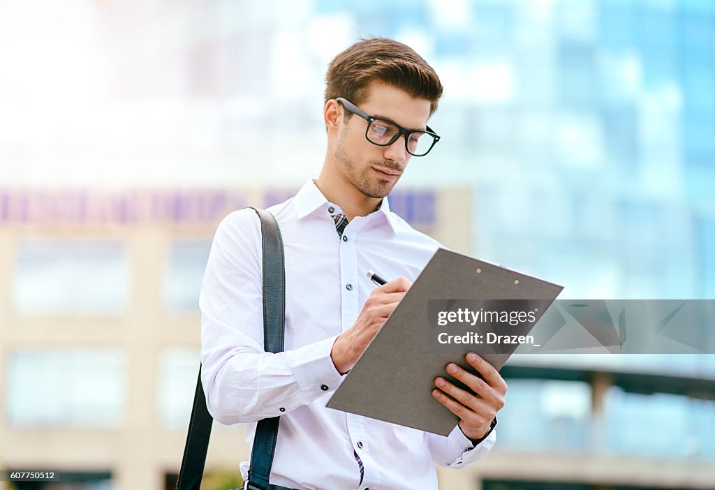 Jovem especialista assinando o documento perto do prédio do escritório