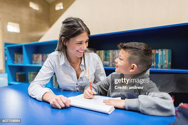 lehrer mit einem schüler in der bibliothek - schulkinder eltern stock-fotos und bilder