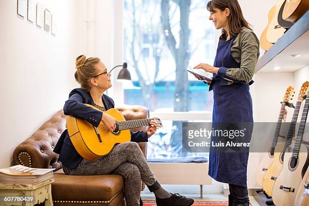 worker looking at customer playing guitar - guitar shop stock pictures, royalty-free photos & images