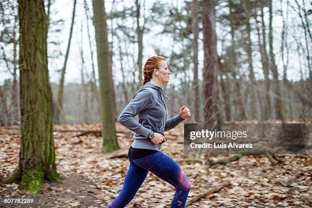 determined woman jogging in forest - hoodie headphones - fotografias e filmes do acervo