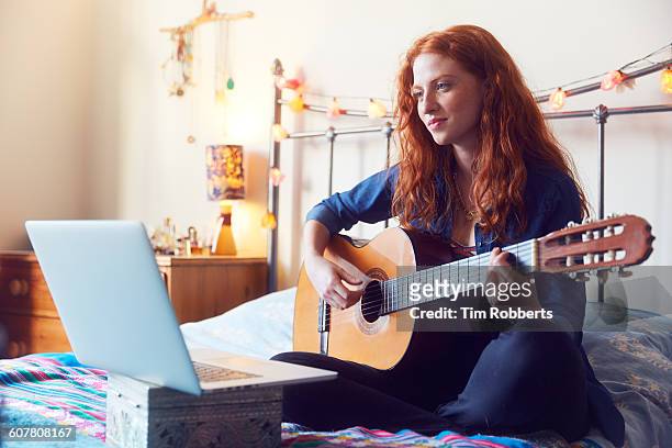 young woman on bed with guitar and laptop - chitarra foto e immagini stock