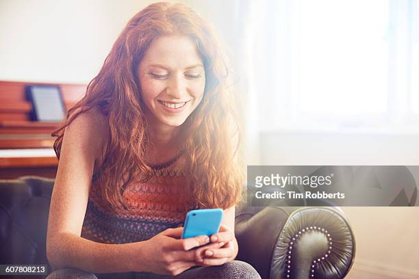 young woman sat with smart phone. - chica salon movil fotografías e imágenes de stock