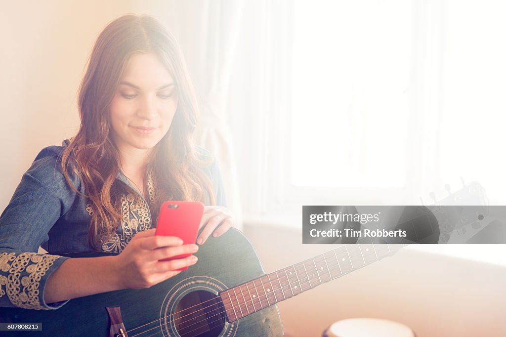 Young woman with guitar and smart phone.