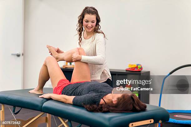 young adult female therapist stretching a female patients leg - postoperatief stockfoto's en -beelden