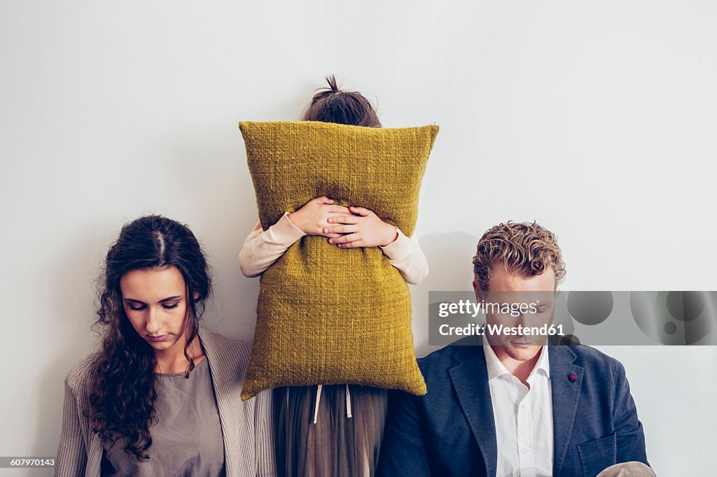 Couple having relationship conflict with their daughter hiding her face behind cushion