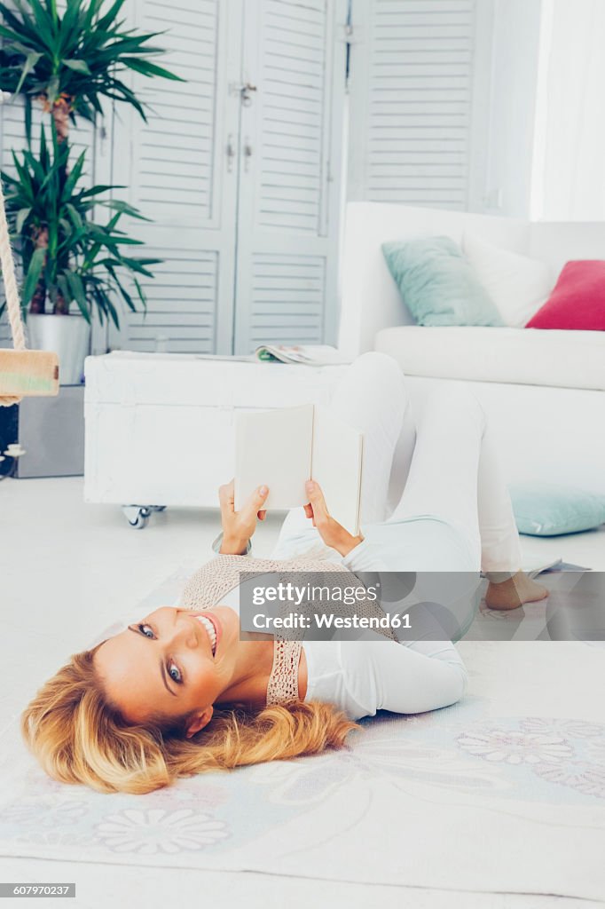 Portrait of smiling blond woman lying on the floor with a book