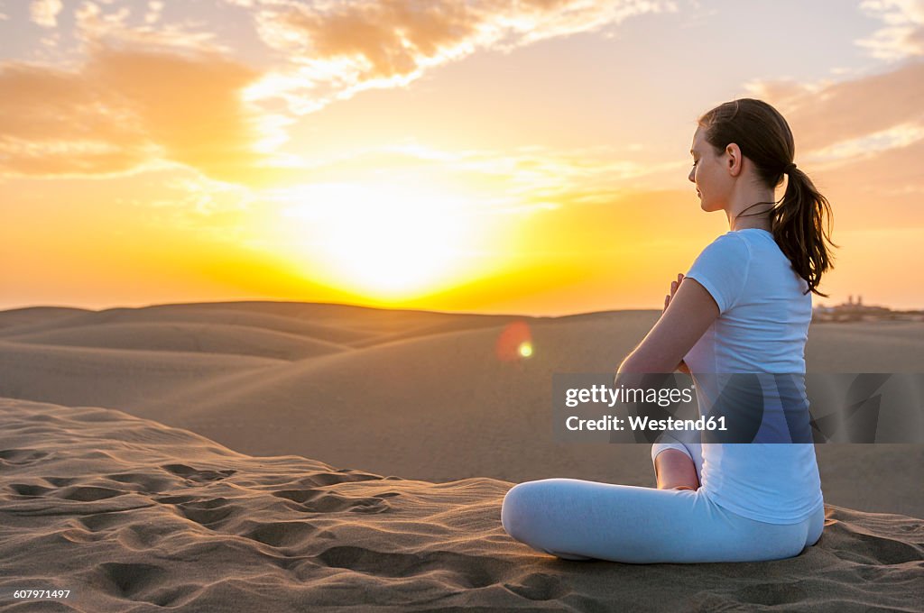 Woman practising yoga on sand dunes