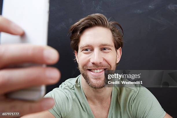 portrait of smiling young man taking a selfie with smartphone - one finger selfie stock-fotos und bilder