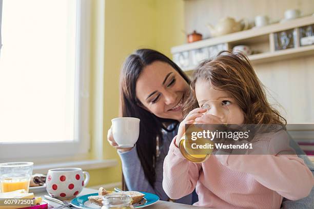 mother and her little daughter together at breakfast table - girl at a table drinking juice stock pictures, royalty-free photos & images