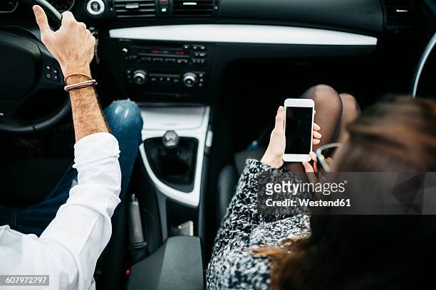 young couple driving in a car, co driver using smart phone - passagerarsäte bildbanksfoton och bilder