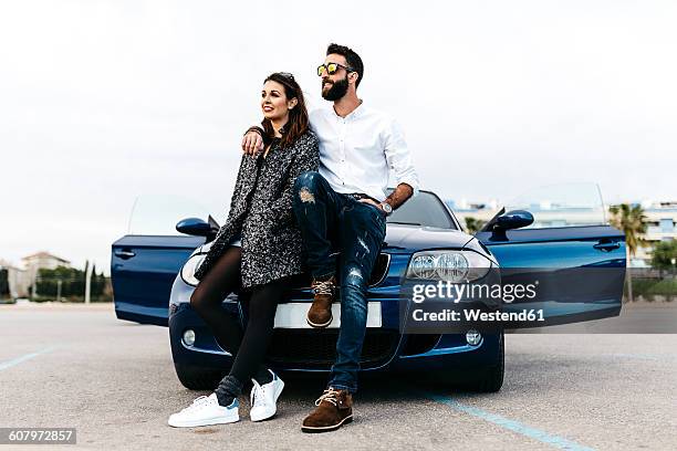 spain, cubelles, young couple sitting on the hood of the car looking at distance - new boyfriend stock pictures, royalty-free photos & images