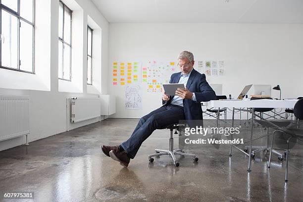 mature businessman sitting in office using digital tablet - office chair stockfoto's en -beelden