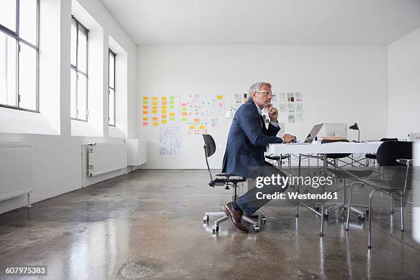 mature businessman sitting in office using laptop - businessman sitting in chair stock-fotos und bilder