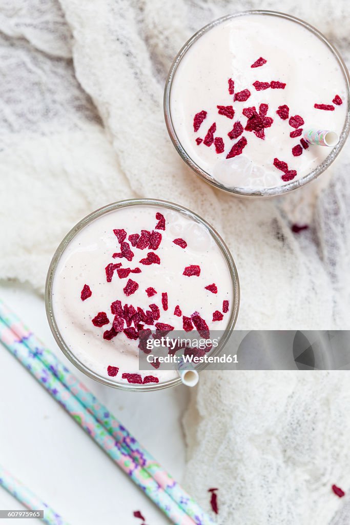 Two glasses of vanilla milkshake with dried raspberries