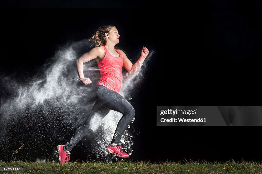 Young woman jogging in a dust cloud in front of black background