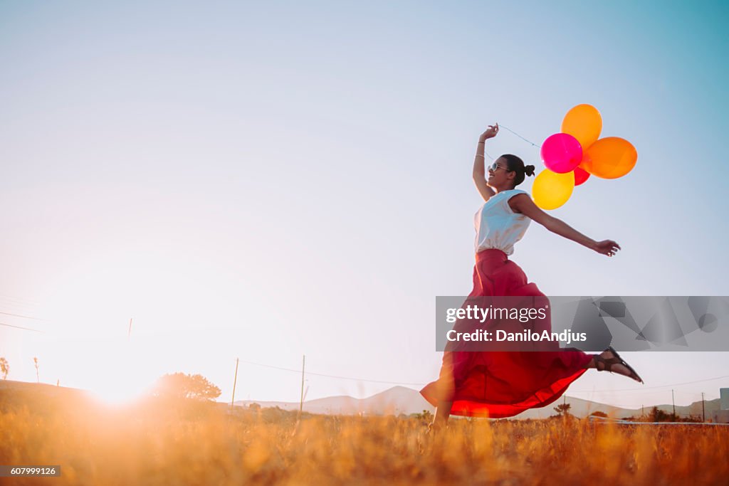 Young woman running threw the fields holding balloons