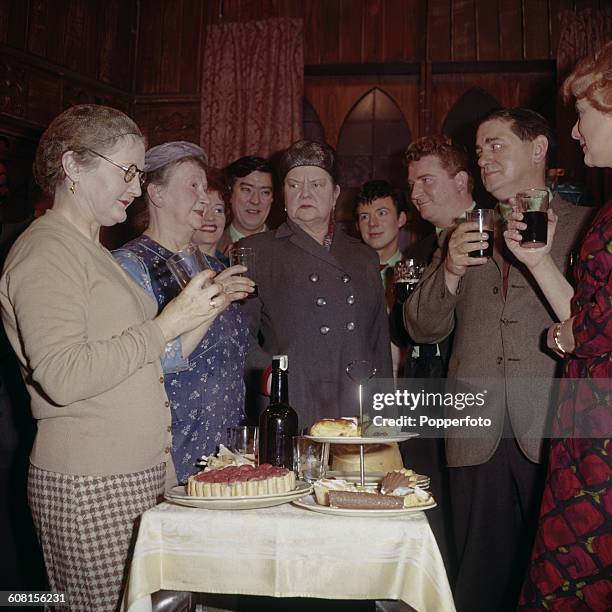 Cast members of the television soap opera Coronation Street pictured together holding drinks around a table of food during a scene on set in...