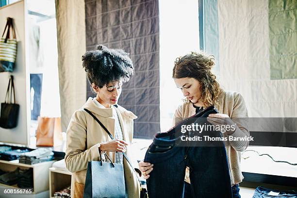 shop owner showing a pair of jeans to customer - shopping candid stock pictures, royalty-free photos & images