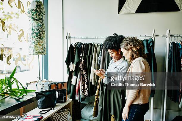 woman showing shop owner photos on smartphone - shopping candid stock-fotos und bilder