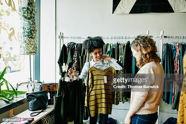 smiling woman showing shop owner clothing options - retail clothing stock pictures, royalty-free photos & images