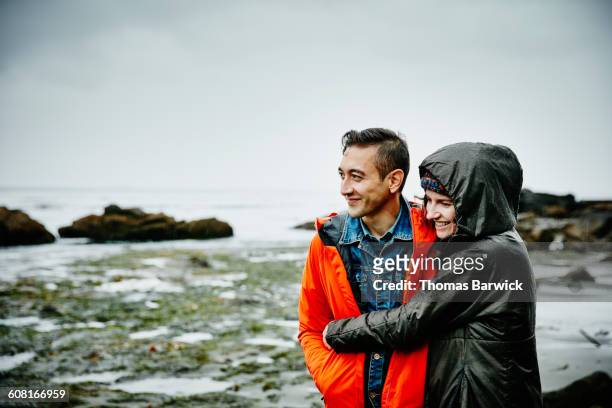 smiling couple embracing on beach - rain couple stockfoto's en -beelden