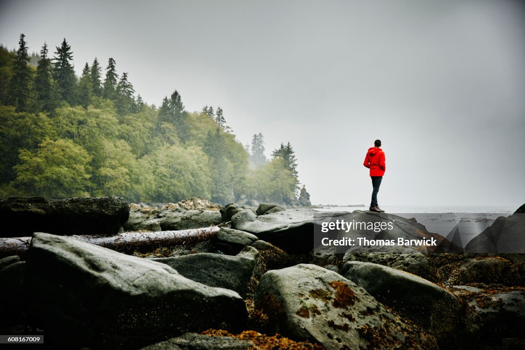 Man standing on boulders on shoreline of ocean