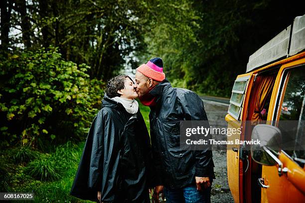 couple on road trip standing next to van kissing - multiracial couple stock-fotos und bilder