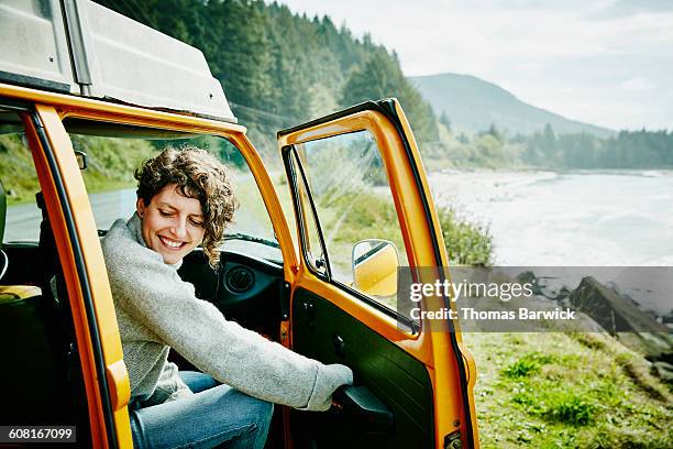 smiling woman on road trip stepping out of van - adventure　sea stock-fotos und bilder