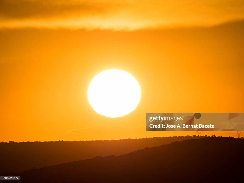 The first plane of a putting Sun, hiding between mountains with wind mills