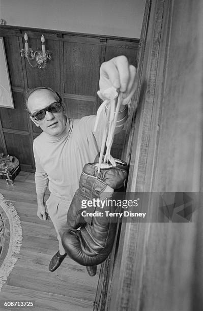 English heavyweight boxer Henry Cooper hangs up his gloves to symbolise his retirement from boxing, UK, 17th March 1971. The day before, he had lost...