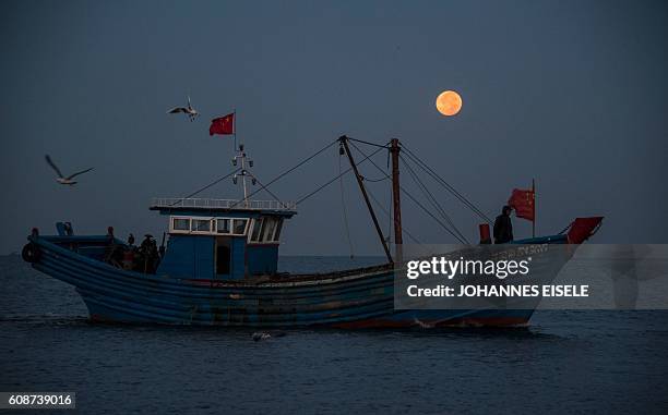 This picture taken on September 17, 2016 shows fisherman on their boat in front of the full moon in Xianrendao in China's northeastern Liaoning...