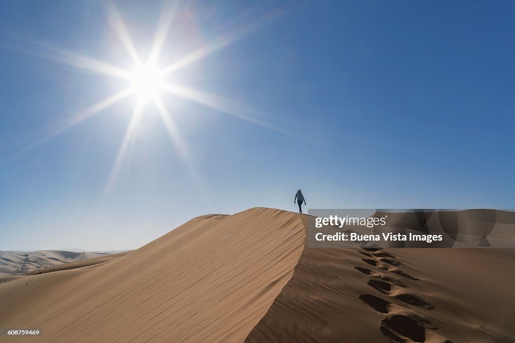 Woman climbing a giant sand dune in a desert