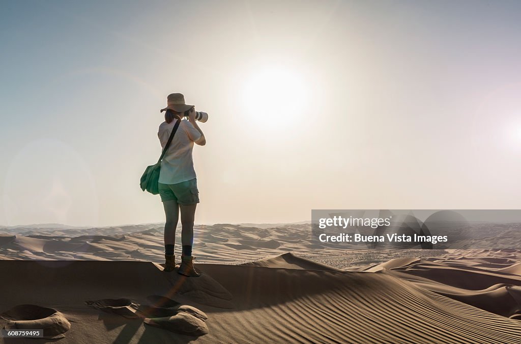 Woman on a sand dune taking pictures of sunset