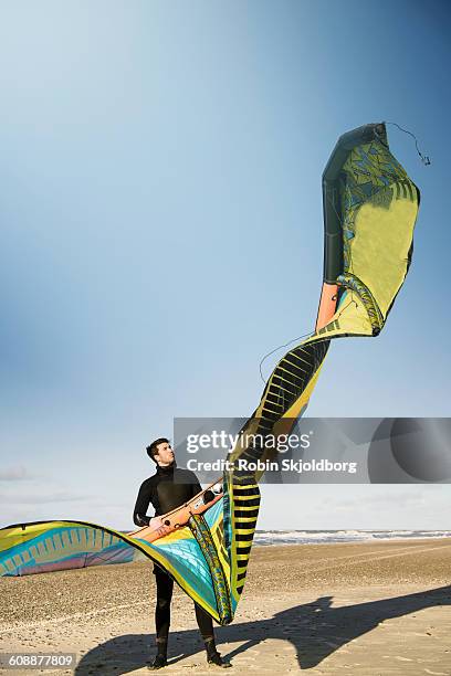 young kitesurfer in wetsuit holding kite on beach - hvide sande denmark stock pictures, royalty-free photos & images