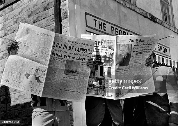 Trio of men read opened copies of the newspapers that announce, in their headlines, President Lyndon Johnson's landslide re-election victory, are...