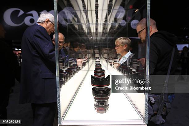 Visitors browse a display case containing a selection of Canon lenses, manufactured by Canon Inc., during the Photokina photography trade fair in...