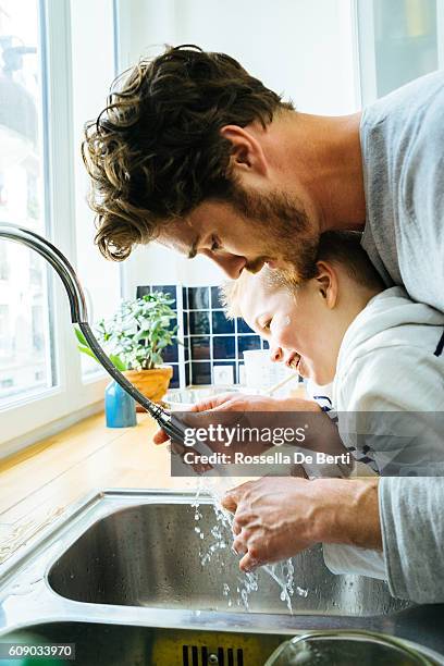 father washing sons hands in kitchen sink after cooking together - kin in de hand stock pictures, royalty-free photos & images