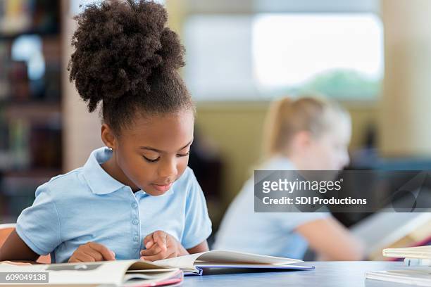 cute african american schoolgirl reading a book in the library - school uniform stock pictures, royalty-free photos & images