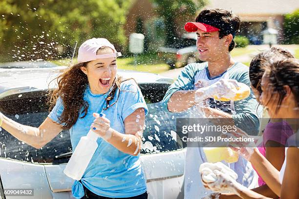 teenage friends have water fight during car wash - carwash stock pictures, royalty-free photos & images