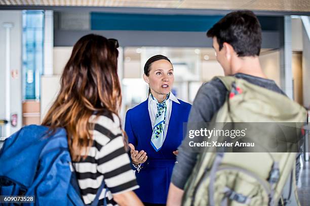 hostess aerea che aiuta giovane coppia in aeroporto - flight attendant serving foto e immagini stock