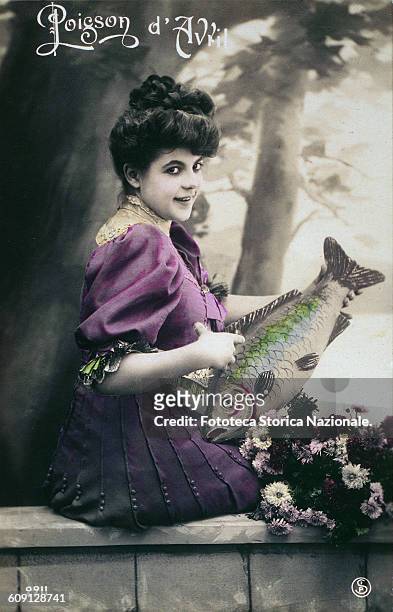 The first April "Poisson D'Avril", cheerful young woman holds with the left hand a big fish hilariously fake, and with the right indicates it with...