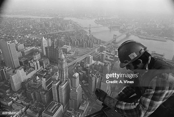 Worker atop the World Trade Center during its construction in New York City, USA, 1971. The Woolworth Building, Brooklyn Bridge and Manhattan Bridge...