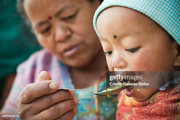 asian woman feeding food to little child. - glimpses of daily life in nepal stock pictures, royalty-free photos & images
