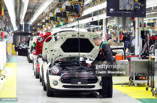 An employee inspects the engine area of a Mini automobile, produced by Bayerische Motoren Werke AG , as it reaches the end of the production line...