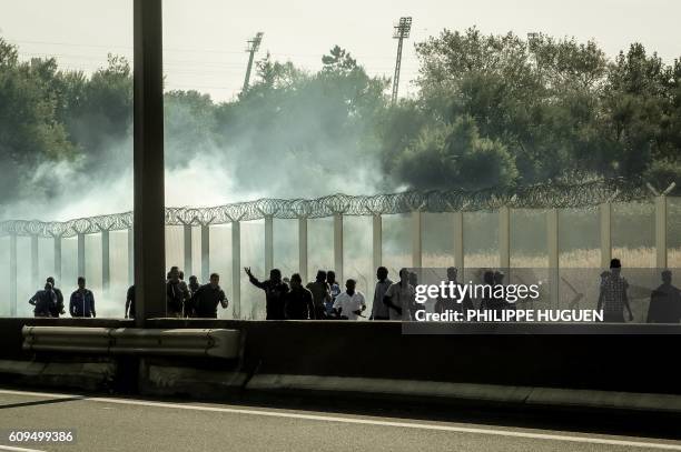 Migrants run away from tear gas during clashes with riot police trying to prevent them from getting into trucks heading to Great Britain, on...