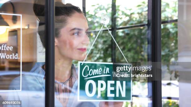 female coffee shop owner opening the shop - store sign stockfoto's en -beelden