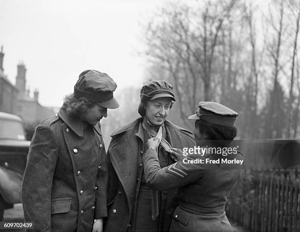 Corporal Hinds of the British Auxiliary Territorial Service shows new recruits, who have just come from the clothing department, how to knot their...